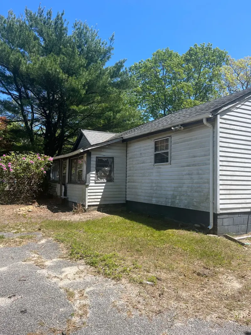 Side of a white ranch beside a gravel driveway, Medford, NY